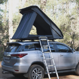 RoofPod Rooftop tent on a silver SUV with ladder in a forest setting