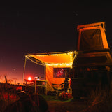 Vehicle with a RoofPod rooftop tent and Awning attached, illuminated with a night sky in the background