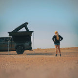 Person standing next to a truck with an open roof top tent and a RoofPod Awning in a desert setting