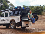 A person sitting on the Front Runner Cargo Bed Slide / Medium fitted to a Camp4x4 vehicle in the out doors