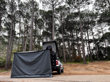 Off-road camping vehicle, in the forest, fitted with a hard shell rooftop tent and an Alu-Cab 270 awning, with the universal side panel in place