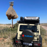 Beige Suzuki Camp4x4 vehicle with a RoofPod SoloPod rooftop tent on a dirt road under a clear blue African sky.