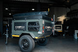 Green camping trailer with 'CAMP4x4' branding inside a warehouse.