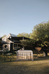 Camper van with rooftop tent in outdoor setting including a two seater camping table and chairs.