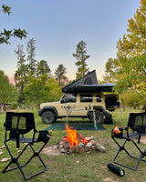 Camper van with rooftop tent parked near a campfire in a forest setting