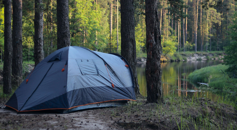 Camping tent set up in a forest near a lake