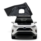 A black iKAMPER Skycamp 4.0 Trio, 3 sleeper, rooftop tent with a window opening is mounted on the roof of a white SUV, shown from the front against a clean white background.