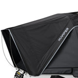 A close-up of a black ikamper tent or cover with a white ikamper logo printed on the side, showing the fabric texture, zipper pulls, and a portion of the support frame against a white background.