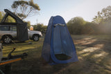 Blue pop-up shower cubicle tent on a grassy field with a vehicle and trees in the background