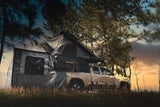 Truck parked in a forest at sunset. Alu-Cab 270 awning, with the Awning Side Wall Kit and a hard shell rooftop tent, fitted to the camping vehicle