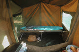 Camping tent interior with stretcher bed, sleeping bag, and personal items.